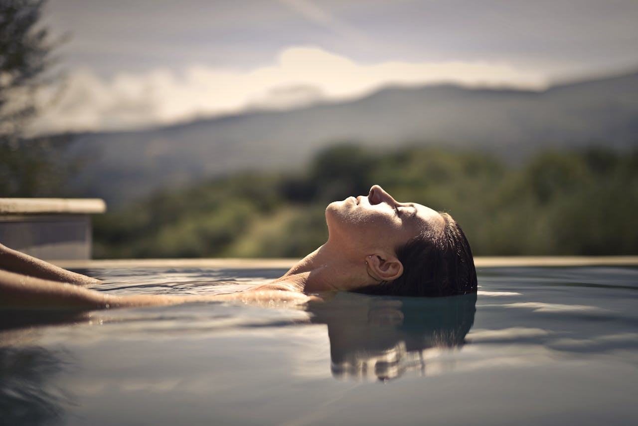 A woman enjoys a serene moment floating in a swimming pool amidst a scenic mountain backdrop.