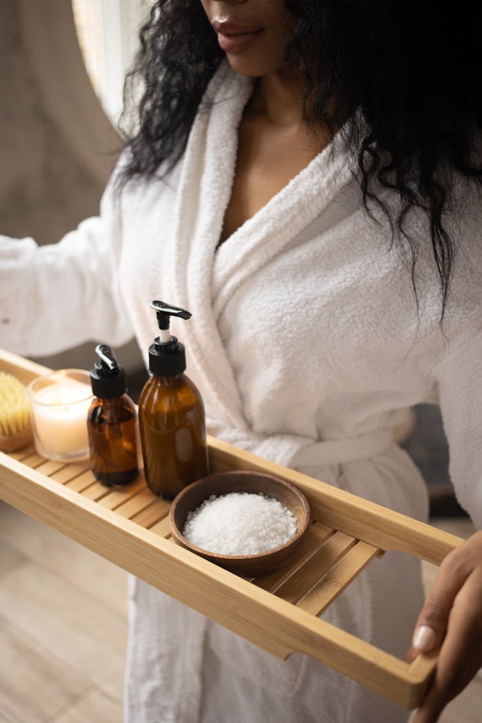 contact-img A woman in a bathrobe holds a tray of natural spa products, focusing on self-care.