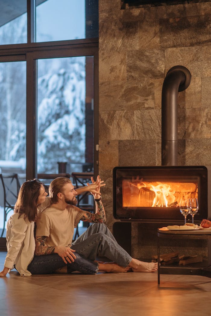 A couple enjoying warmth beside a roaring fireplace in a winter setting.